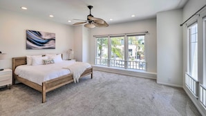 Une chambre à coucher avec un lit, un ventilateur de plafond, une fenêtre donnant sur un beau paysage et un tableau accroché au mur.