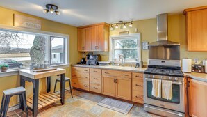 A kitchen with wooden cabinets, a stainless steel stove, and a window overlooking a snowy landscape.