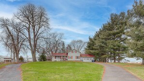 A two-story house with a red roof and white siding, surrounded by a grassy yard and trees.
