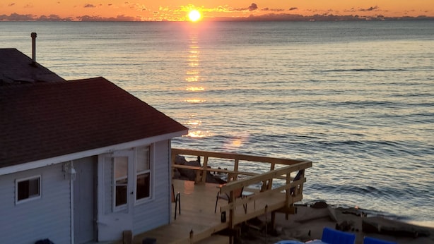 Una casa costera con una terraza de madera que da al mar, con un pequeño barco amarrado cerca.