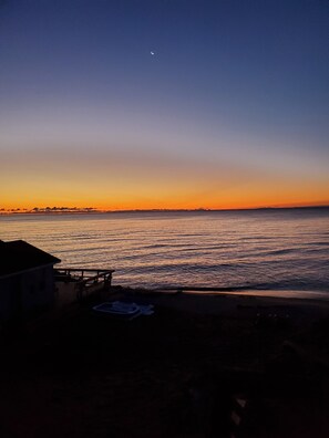Vista de playa con atardecer, mar tranquilo y un edificio pequeño al frente.