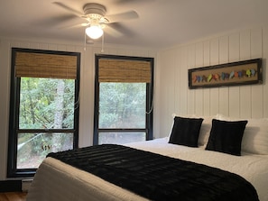 A bedroom with a large bed, two windows with blinds, a ceiling fan, and a wall-mounted bird decoration. - Holly Forest Treehouse - Dogs Welcome! (Sapphire)
