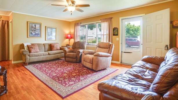 A living room with a ceiling fan, a large window with curtains, a brown leather couch, a beige sofa, and a patterned rug. - Welcoming Biggers Home - Great Duck Hunting! (Biggers)