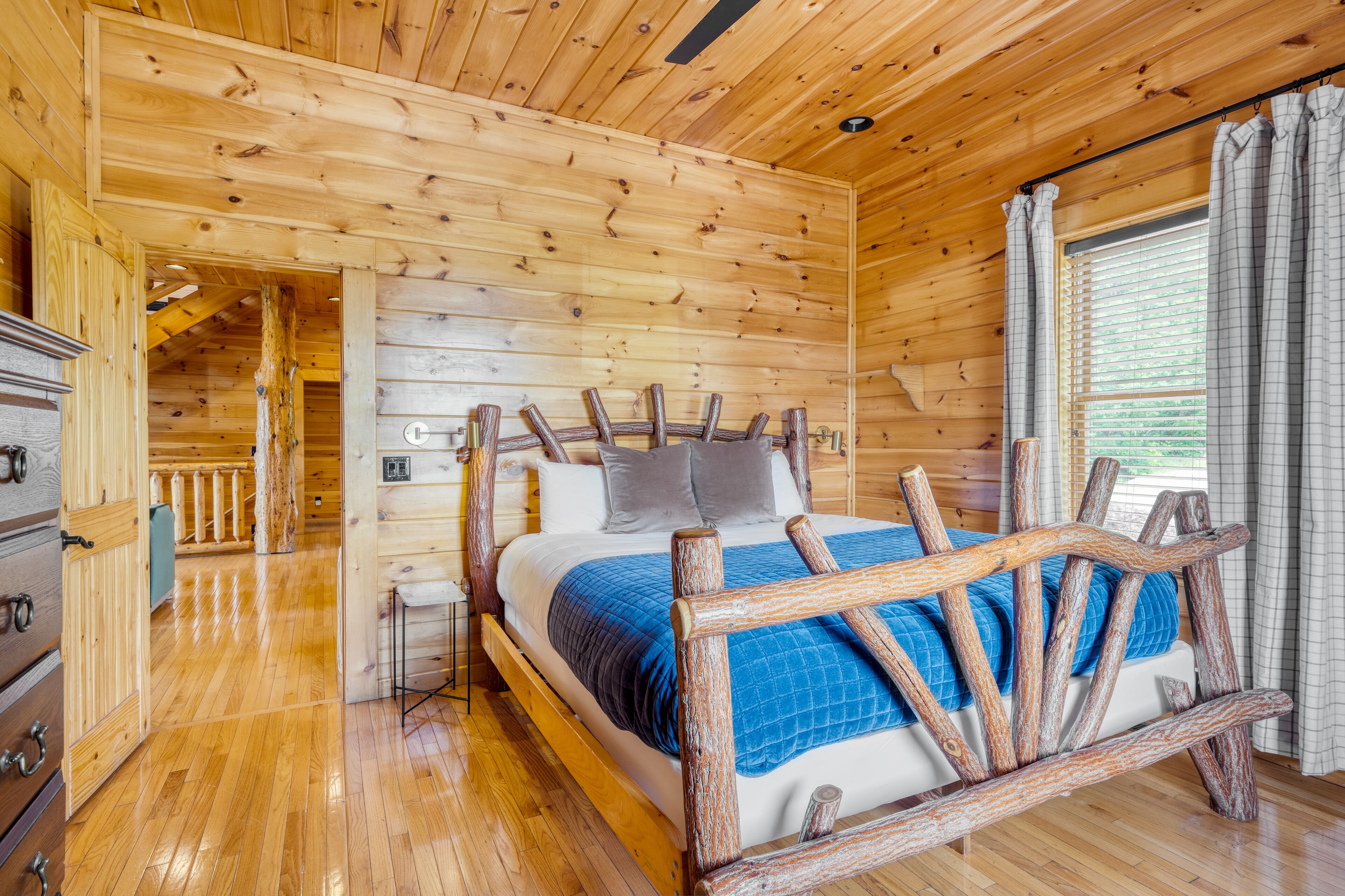 Un dormitorio de cabaña de madera con cama, cabecera de madera y ventana con cortinas.