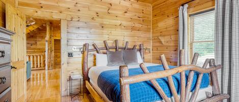 Un dormitorio de cabaña de madera con cama, cabecera de madera y ventana con cortinas.
