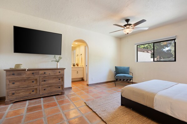 A bedroom with a bed, a dresser, a chair, a ceiling fan, and a window.