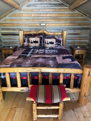 A log cabin bedroom with a bed featuring a quilt with 'ADVENTURE' text, wooden headboard, and bench. - Retreat to our cozy cabin nestled in a private hideaway.
Solar lights & shower (Marion)