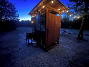 A small wooden cabin with a sink and a table, surrounded by trees and a picnic table in the background. - Retreat to our cozy cabin nestled in a private hideaway.
Solar lights & shower (Marion)