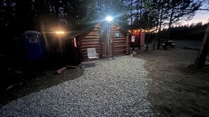 Een rustieke hut met een grindpad dat naar de ingang leidt, omringd door bomen.