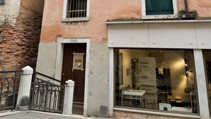 Un edificio de varios pisos con fachada color beige, múltiples ventanas con contraventanas y una entrada a nivel de calle con una puerta marcada '5614'.