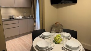Comedor con una mesa dispuesta para cuatro, cocina al fondo y un televisor montado en la pared.