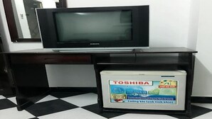 A black TV on a black desk with a Toshiba box underneath. - Hoang Nam Hotel by Zuzu (Ho Chi Minh Municipality)