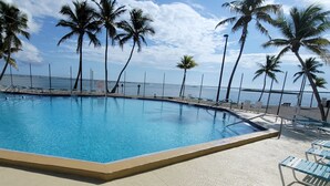 Una piscina con vista al océano, rodeada de palmeras y sillas de playa.