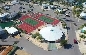 An aerial view of a sports complex with a tennis court, basketball court, and a covered pavilion.