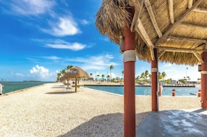 A beach with a thatched-roof structure, palm trees, and a clear blue sky. - RV resort site/rvsite/spot/lot Cudjoe Florida mm23 Key West MONTHLY DISCOUNT (Cudjoe Key)