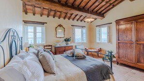 A bedroom with a large bed, wooden ceiling beams, a dresser, a mirror, and a view of the sea through the windows. - Tuscan Fizz Villa a Vineyards Retreat (Capannori)