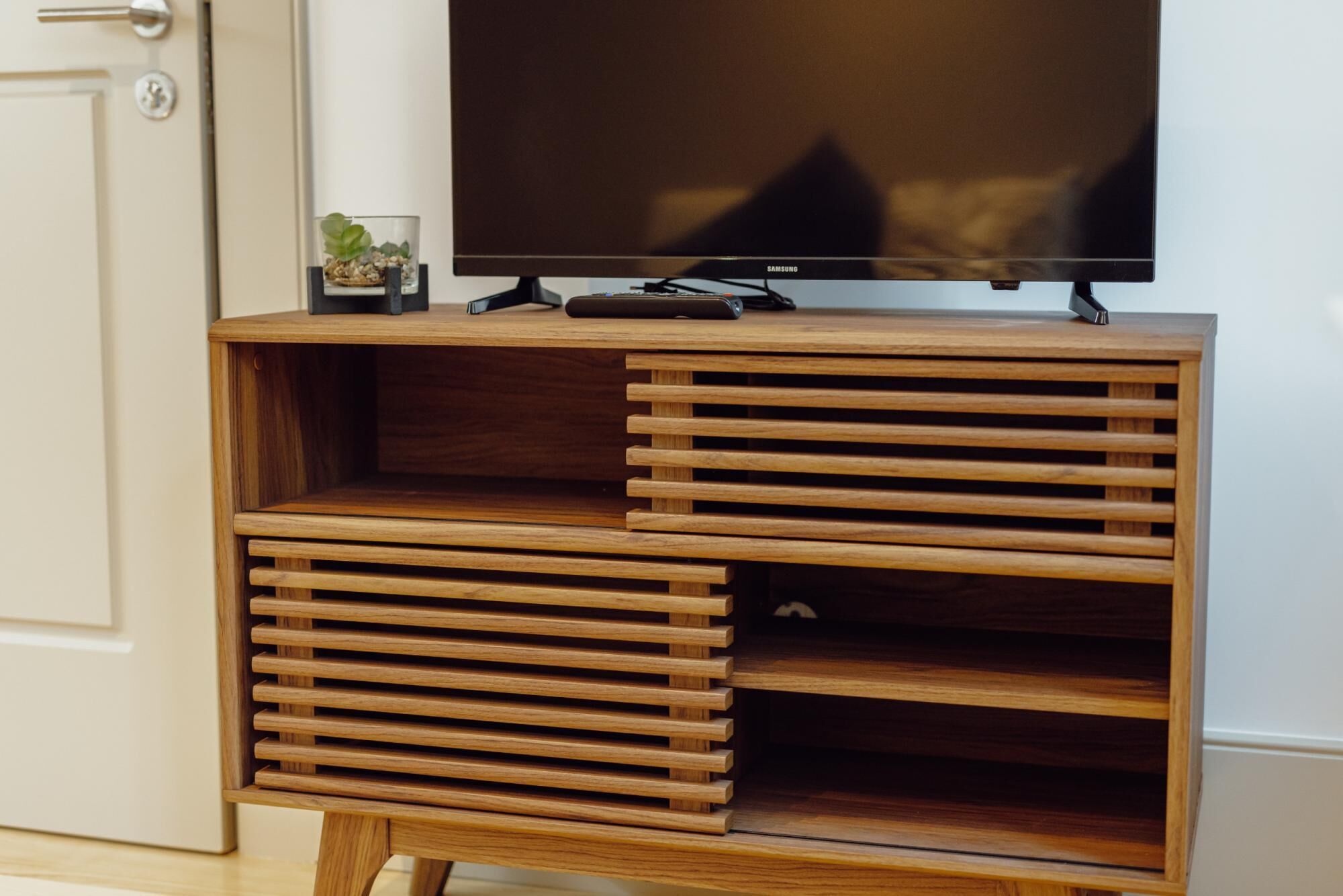 Un mueble de madera para entretenimiento con un televisor de pantalla plana, una planta pequeña y un control remoto.