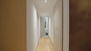 A narrow hallway with wooden flooring and white walls, leading to a bathroom with a sink and mirror. - Legacy Oporto Design Apartment A by Vacationy (Porto)