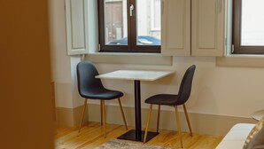 A small dining area with a table and two chairs, a window with a view of the street, and a wooden floor. - Legacy Oporto Design Apartment A by Vacationy (Porto)