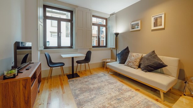 A modern living room with a sofa, two chairs, a small table, a TV, and a window with curtains. - Legacy Oporto Design Apartment A by Vacationy (Porto)