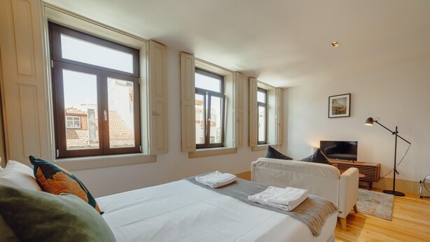 A bedroom with a large bed, two windows, a TV, and a desk.