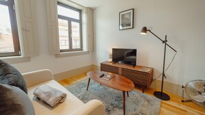 A modern living room with a sofa, a coffee table, a TV on a wooden stand, a floor lamp, and a fan.
