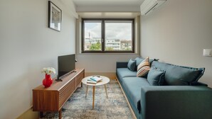 En moderne stue med en sofa, et fjernsyn, et lille bord og en rød vase.