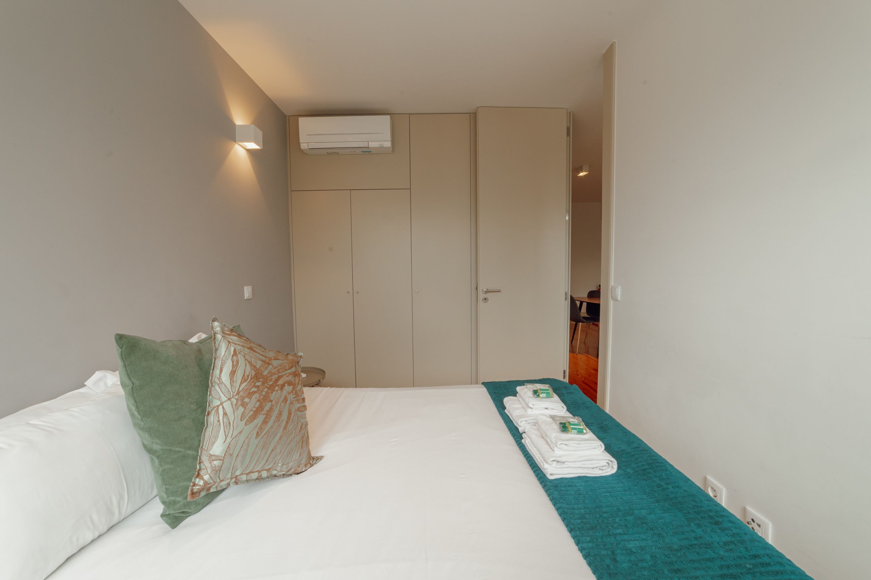 Ein Hotelzimmer mit Bett, Kissen, einer türkisfarbenen Decke, einem gefalteten Handtuch, einer Klimaanlage und einem Kleiderschrank.