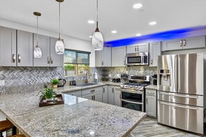 Una cocina moderna con encimeras de granito, electrodomésticos de acero inoxidable e iluminación colgante.