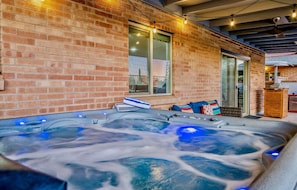 Un bain à remous avec un mur en briques en arrière-plan, une porte en verre et des guirlandes lumineuses.