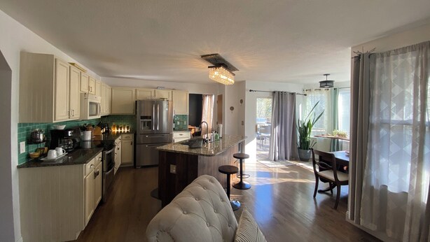 A modern kitchen with white cabinets, a central island, and a dining area with a table and chairs.