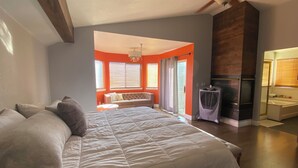 A bedroom with a large bed, a ceiling fan, and a view of a living area with a sofa and a fireplace.