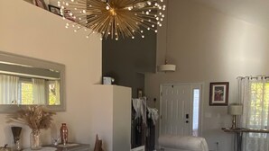 A modern dining area with a long wooden table, a chandelier, and a view of the kitchen.