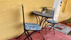 Un patio con dos sillas, una mesa, una planta en maceta y una puerta con una lámpara.
