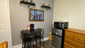 Una cocina compacta con una mesa de comedor, sillas, un refrigerador, un microondas y una guitarra.