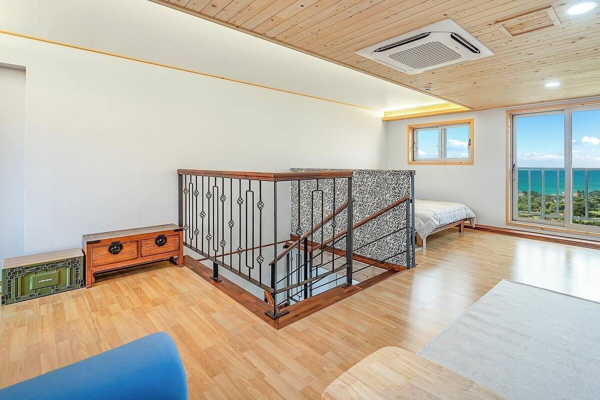 A spacious room with a large window, a bed, a TV, and a staircase with a railing.
