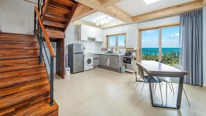 A modern kitchen with a view of the ocean, wooden staircase, and a dining area with a table. - Jeju Hoyeongfarm Stay (Jeju City)