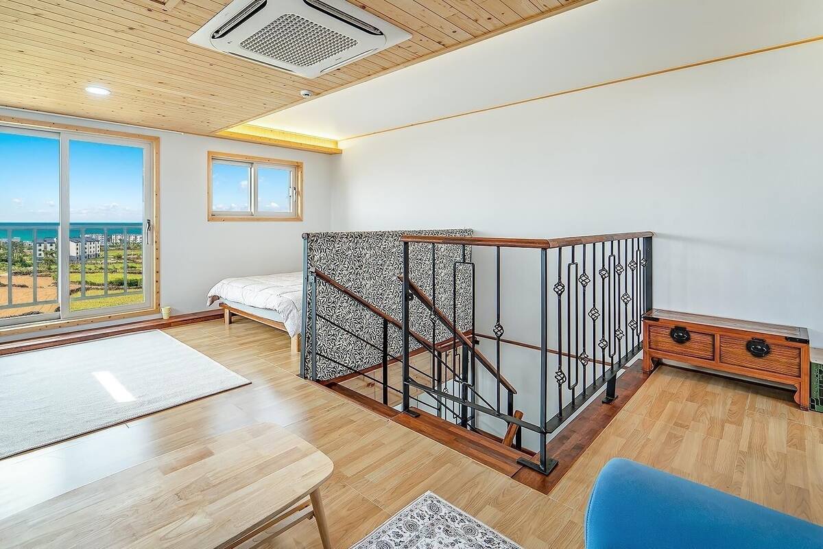 A bedroom with a bed, a TV, a desk, and a balcony with a view.