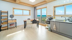 A modern kitchen with a large window, a dining area with a table and chairs, and a view of the sea. - Jeju Hoyeongfarm Stay (Jeju City)