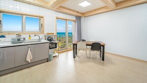 A modern kitchen with a view of the sea, a dining area with a table and chairs, and a large window with curtains. - Jeju Hoyeongfarm Stay (Jeju City)