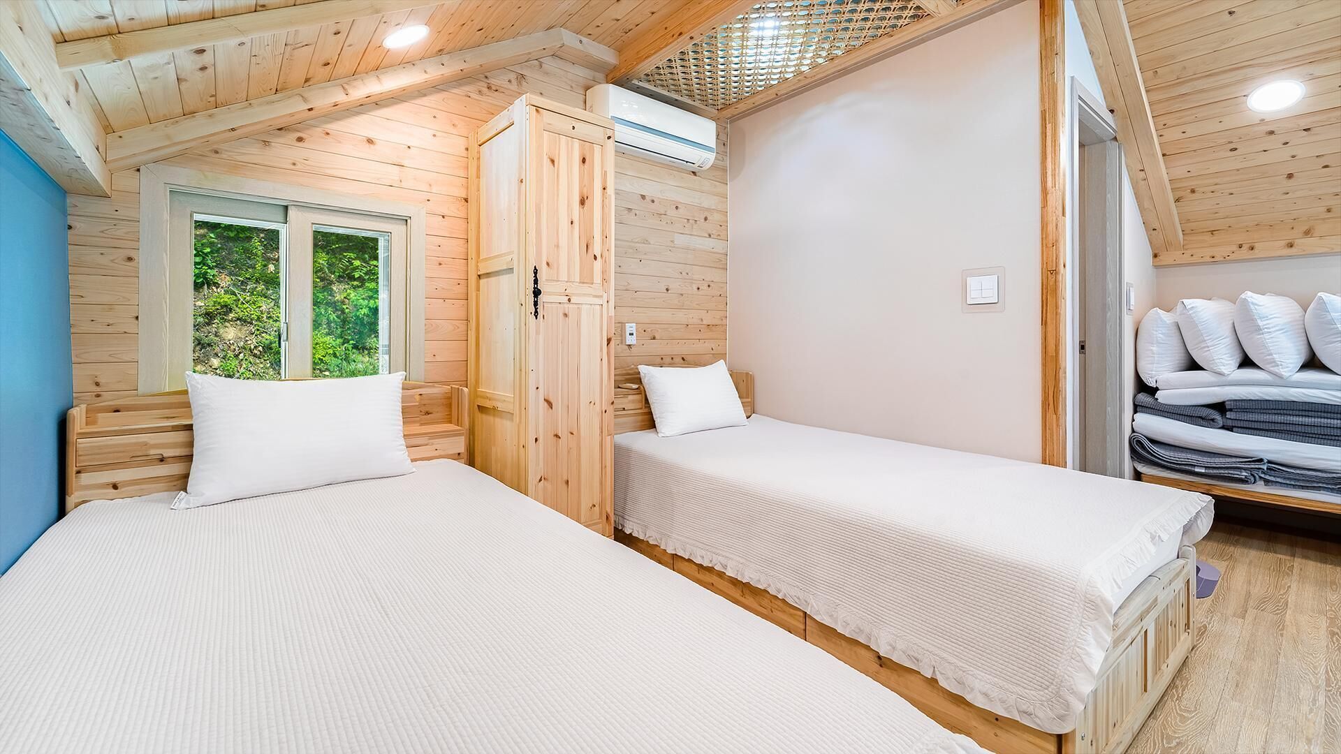 Una habitación con dos camas, una ventana que da a zonas verdes y un equipo de aire acondicionado.