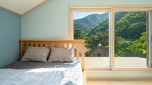 Une chambre à coucher avec un lit, une tête de lit en bois et une grande fenêtre donnant sur une montagne et une maison.