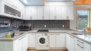A modern kitchen with white cabinets, a built-in dishwasher, a washing machine, and a black tiled backsplash.