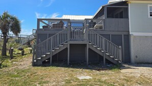 A two-story building with a staircase leading to a balcony, surrounded by a grassy area and palm trees. - Beach front cottage - don't let the outside fool you - check out the photos!  (Fernandina Beach)