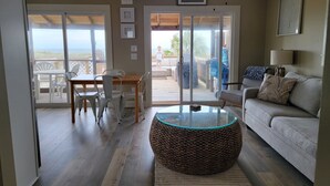 A spacious living room with a glass coffee table, a woven ottoman, a grey sofa, and a ceiling fan. - Beach front cottage - don't let the outside fool you - check out the photos!  (Fernandina Beach)
