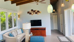 A living room with a wooden ceiling, a ceiling fan, a TV, a sofa, a lamp, and a wall art piece.