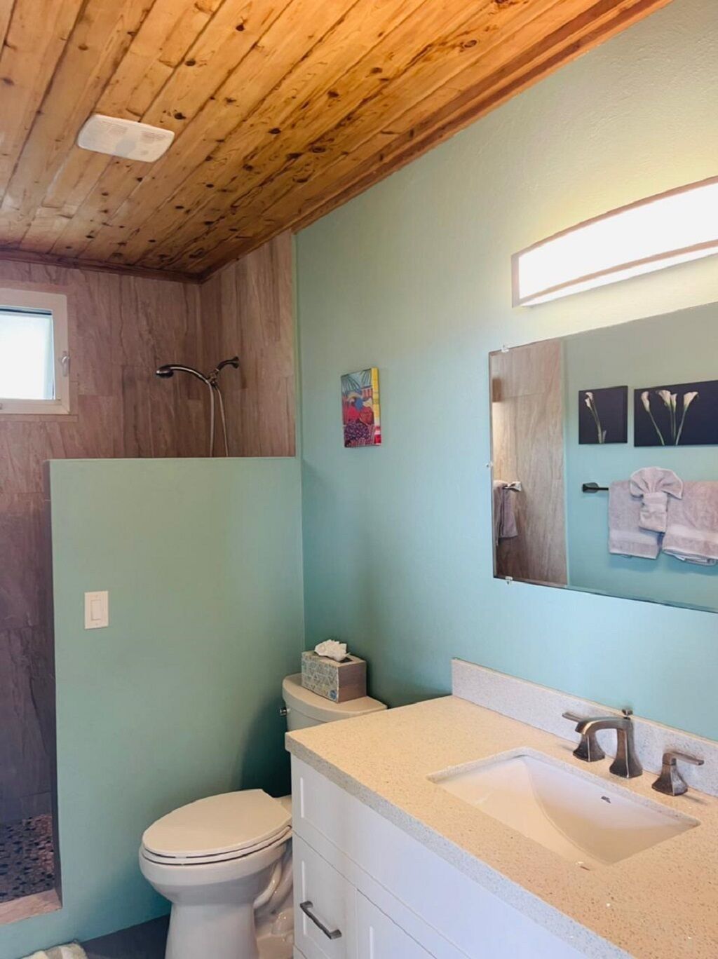 A bathroom with a wooden ceiling, a toilet, a sink, and a shower.