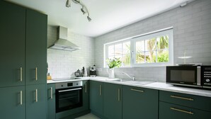 A kitchen with dark green cabinets, a white countertop, a built-in oven, a microwave, and a window with a view of greenery. - Kirrary Townhouse 4 bedroom house VRBO (Dingle)