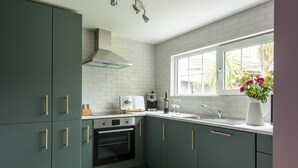 A modern kitchen with dark green cabinets, a built-in oven, a window with a view of greenery, and a vase with flowers on the counter. - Kirrary Townhouse 4 bedroom house VRBO (Dingle)