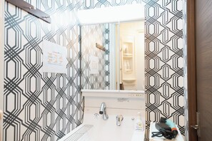 Ein Badezimmer mit Wand in geometrischem Muster, einem Waschbecken mit Wasserhahn und einem Spiegel.